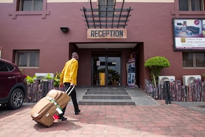 A reception area with a sign above the entrance, a man pulling a suitcase, and air conditioning units on the building's exterior.