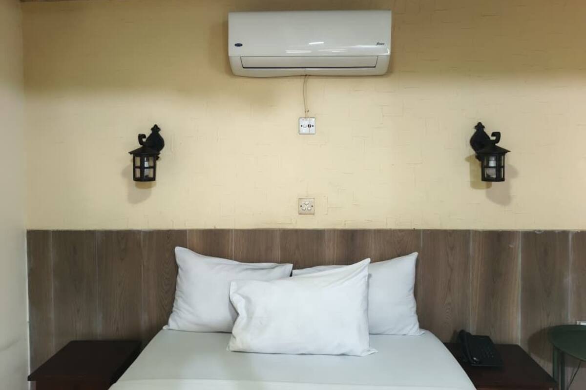 Une chambre d’hôtel avec un lit, des oreillers blancs, une tête de lit en bois, un appareil de climatisation et deux lanternes fixées au mur.