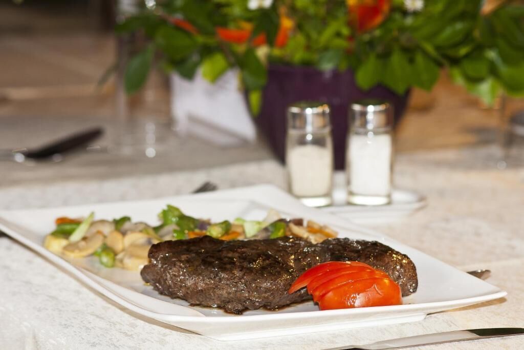 Egy márvány asztalon egy tányér, rajta grillezett hús és zöldségek, egy kés, valamint só- és borsszóró.