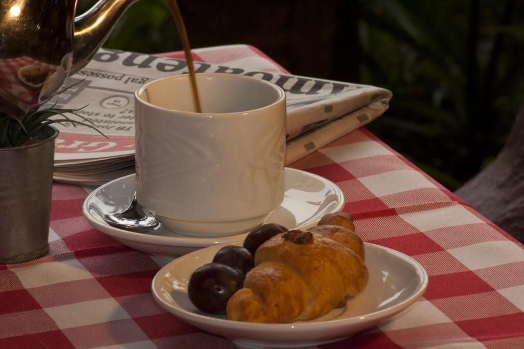 A table with a newspaper, a cup of coffee, a croissant, and a plate with olives.