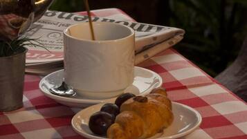A table with a newspaper, a cup of coffee, a croissant, and a plate with olives.