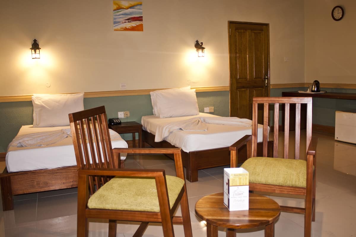 Une chambre d’hôtel avec deux lits, des chaises en bois, une petite table et un tableau au mur.