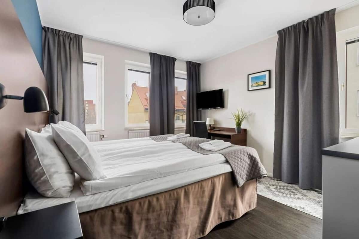 A modern hotel room with a large bed, a desk, a flat-screen TV, and a window with curtains.