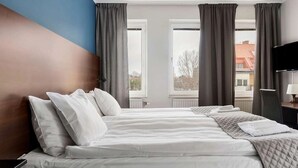 A hotel room with a large bed, two windows, a television, and a desk with a lamp. - Best Western Hotel Solna (Solna)