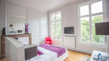 Une chambre à coucher avec un lit, un fauteuil rouge, une télévision et de grandes fenêtres.