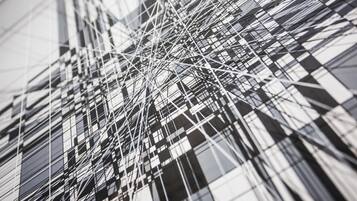 A modern building with a complex network of intersecting lines and reflective glass windows.