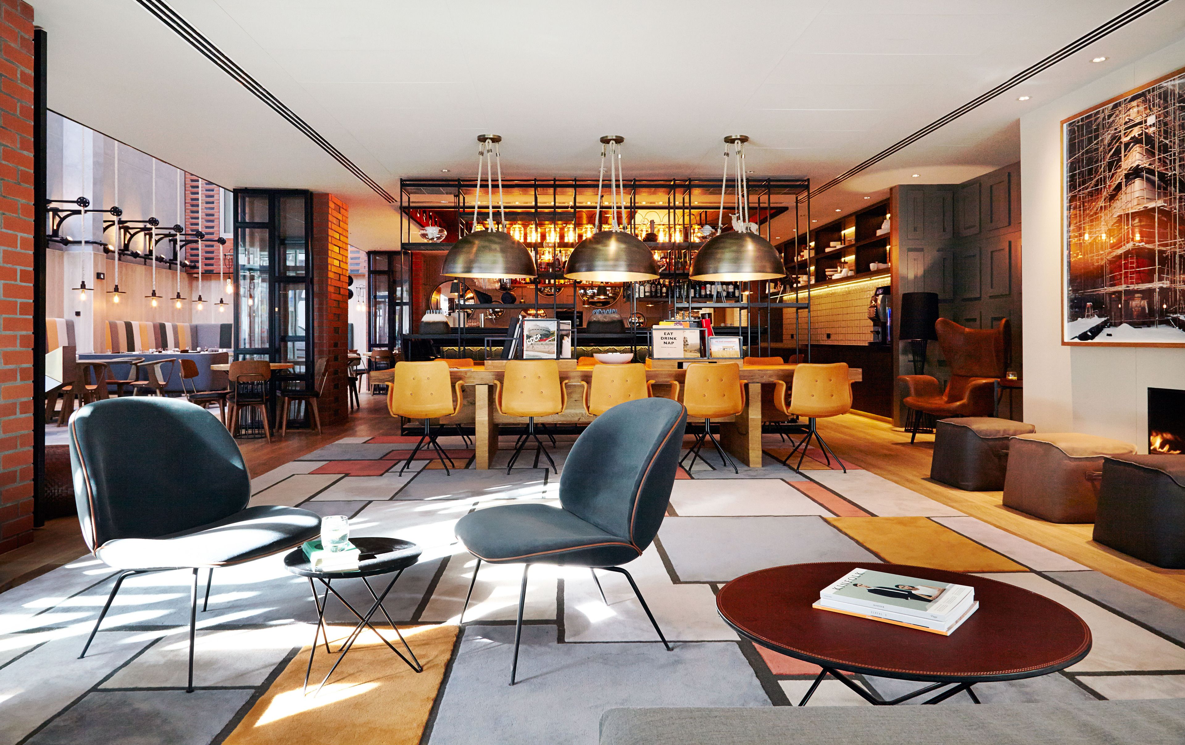 A modern hotel lobby with a bar area, seating arrangements, and a fireplace.