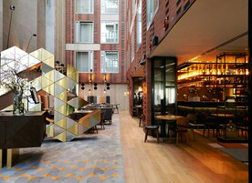 A modern hotel lobby with a bar area, seating arrangements, and a decorative geometric wall.