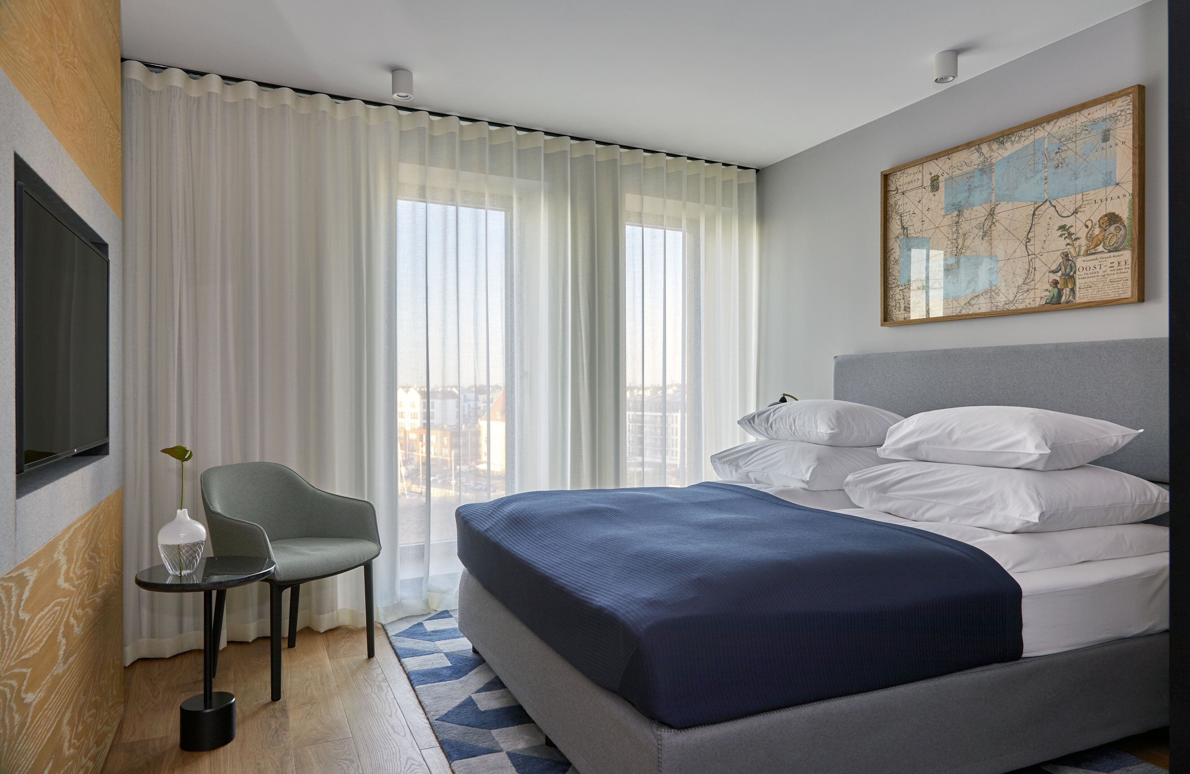 Una habitación de hotel moderna con una cama grande, una mesita pequeña, una silla y un mapa en la pared.