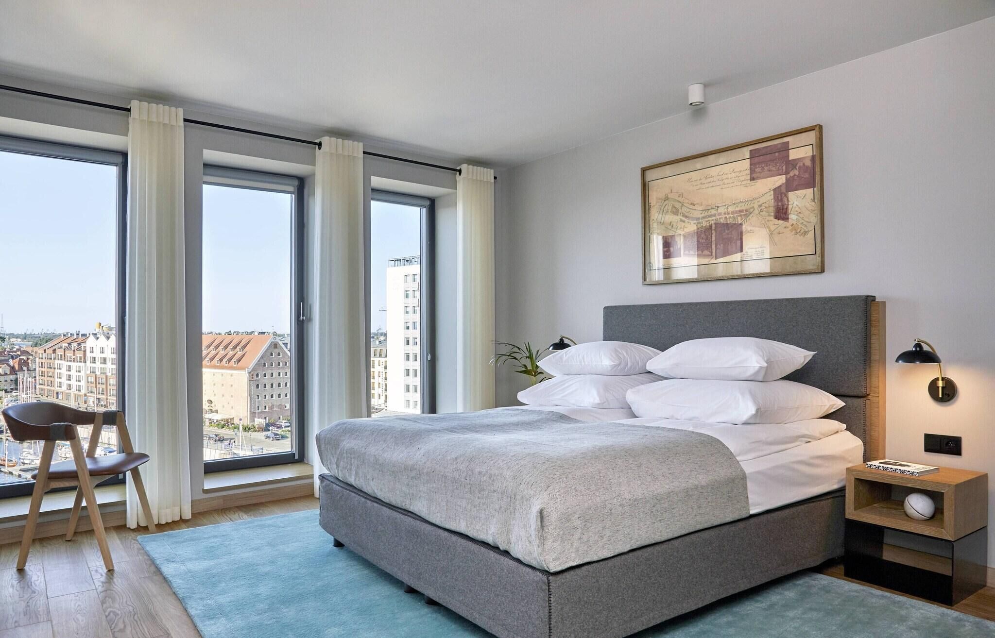 Un dormitorio moderno con una cama grande, una silla, un escritorio y vistas a la ciudad.