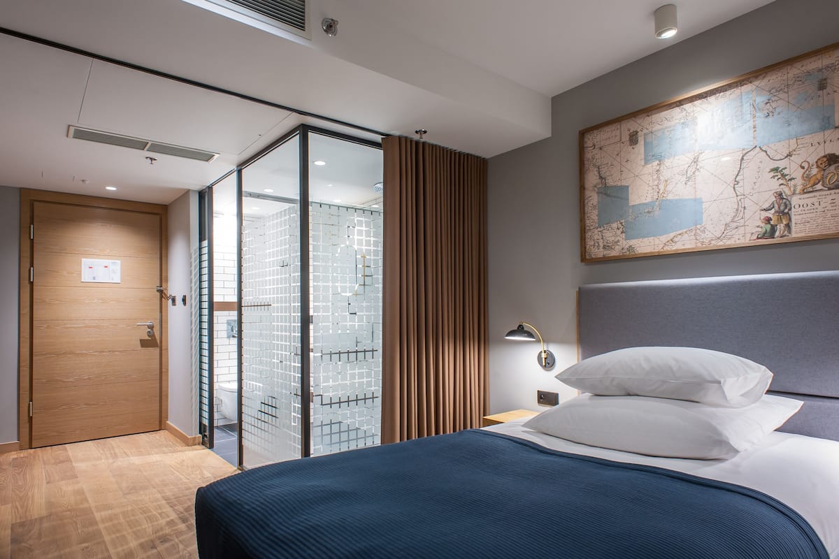 A modern hotel room with a large bed, a map on the wall, and a sliding glass door leading to a shower area.