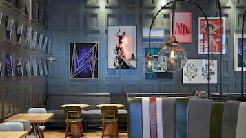 Un intérieur moderne avec un espace salon, des tables en bois et un mur décoré d’œuvres d’art encadrées.