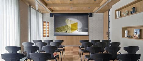 A conference room with a modern design, featuring a wooden ceiling, black chairs arranged in rows, and a large screen displaying a yellow geometric design.