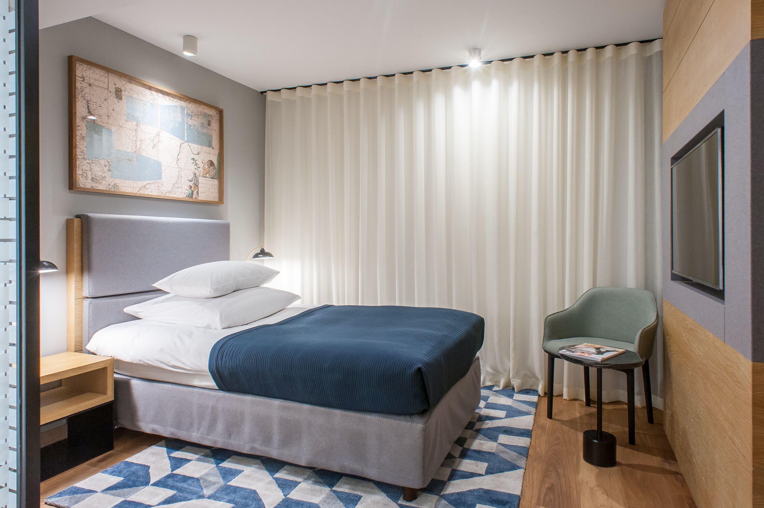 Et moderne hotelværelse med en stor seng, et kort på væggen, en stol og et lille bord.