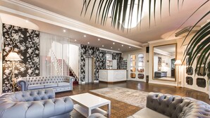 A spacious living room with a large sofa, a coffee table, and a fireplace. There is a kitchen area in the background with a white countertop and various kitchen items. - Hotel Meeting (Cesenatico)