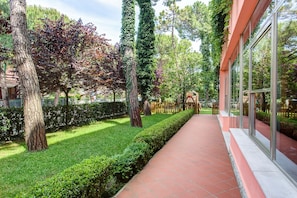 A well-maintained garden with a paved walkway, neatly trimmed hedges, and tall trees. - Hotel Meeting (Cesenatico)