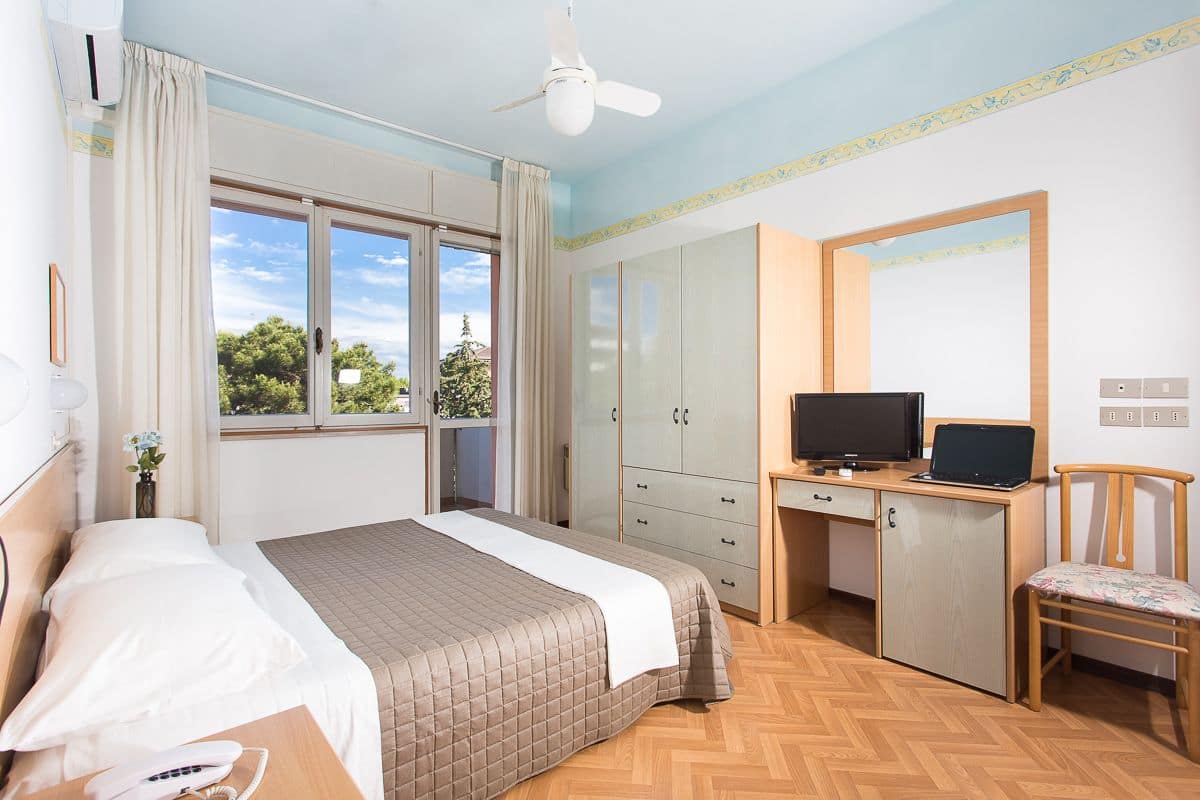 Una habitación de hotel con una cama, un escritorio con una computadora portátil, un televisor y una silla.