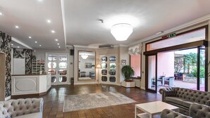 A hotel lobby with a reception desk, seating area, and large windows offering a view of the outdoor patio. - Hotel Meeting (Cesenatico)
