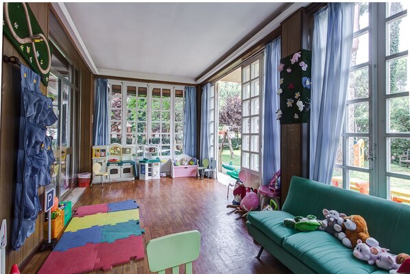 A spacious room with large windows, a green sofa, and children's play area. - Hotel Meeting (Cesenatico)