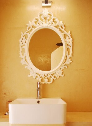 A bathroom with a white sink, a gold-colored wall, and an ornate white mirror. - Samothraki Beach Apartments and Suites Hotel (Samothrace)
