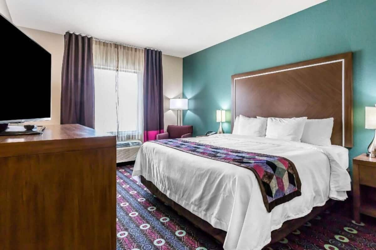 A hotel room with a large bed, a desk, a chair, a TV, and a window with curtains.