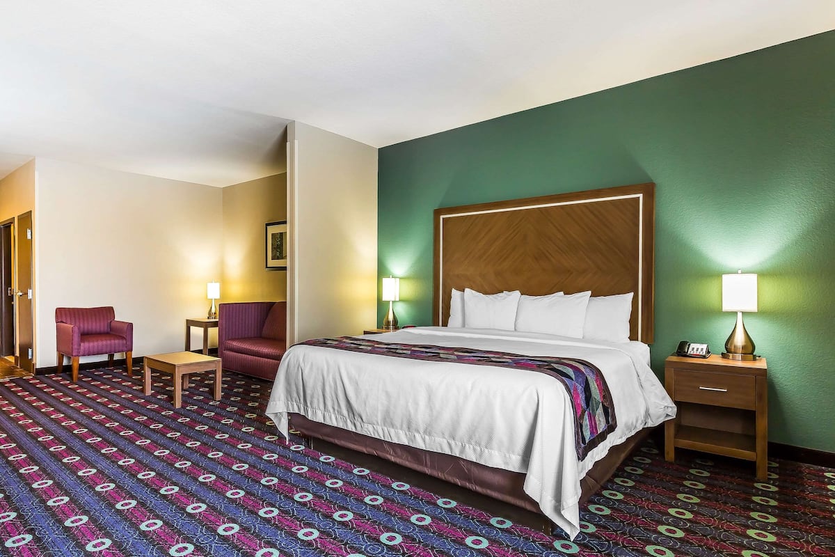 A hotel room with a large bed, two chairs, a small table, and a nightstand with a lamp.