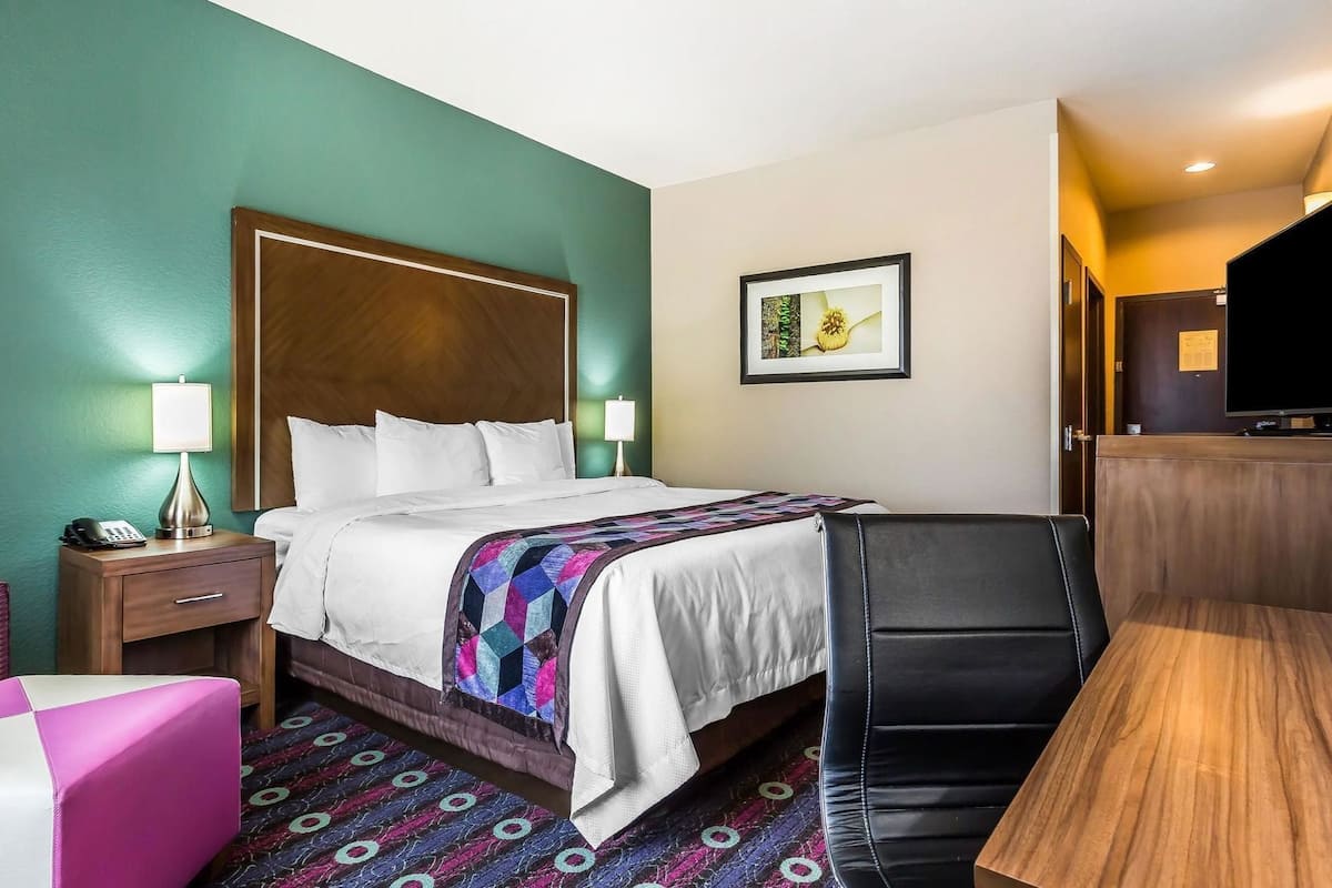 A hotel room with a bed, a desk, a chair, a phone, and a TV.