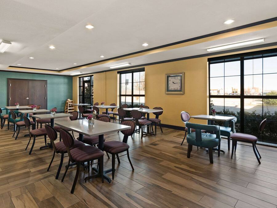 Uma sala de jantar espaçosa com várias mesas e cadeiras, grandes janelas com vista e um relógio na parede.