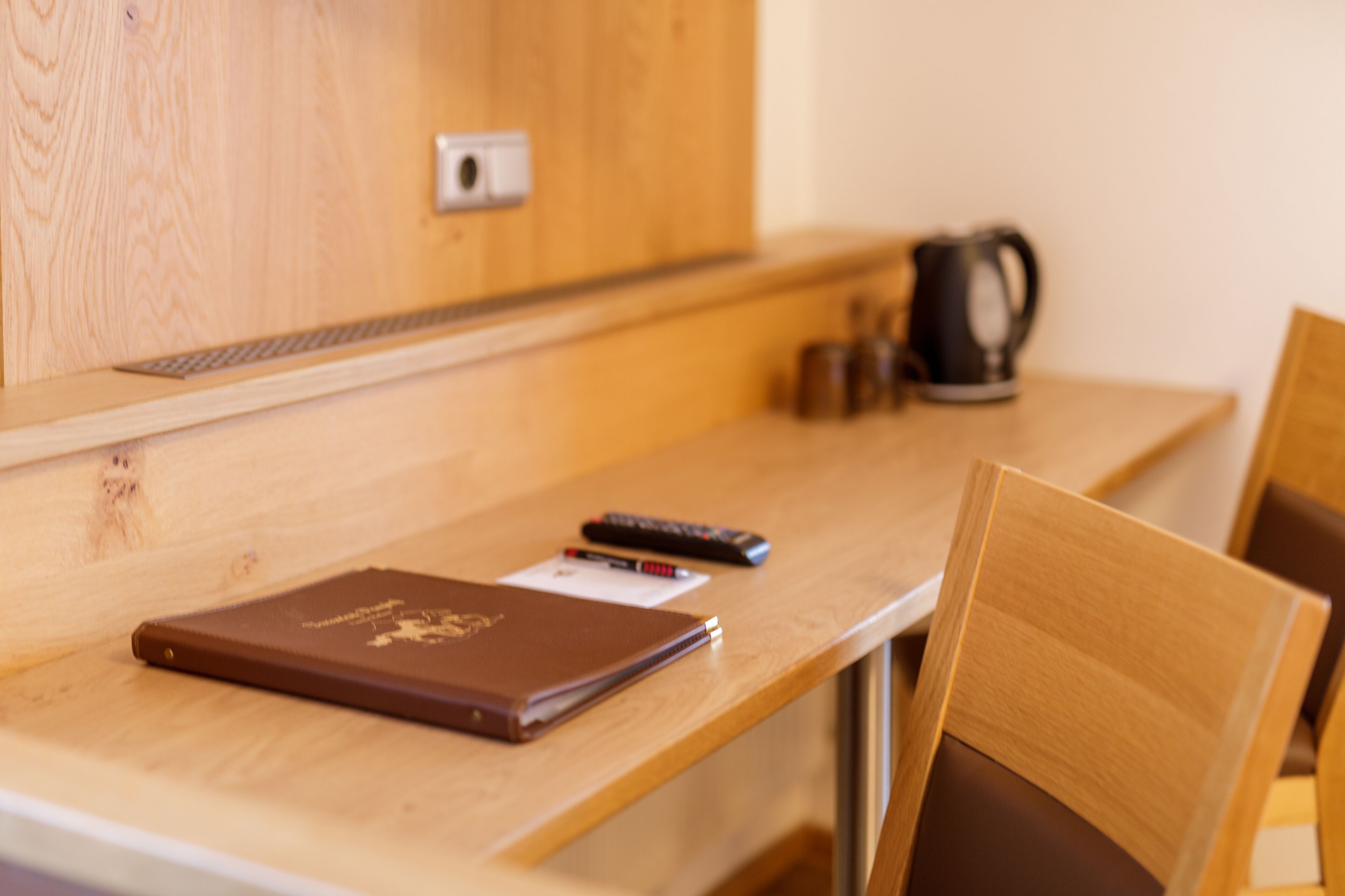 A wooden desk with a laptop, a remote control, and a notebook.