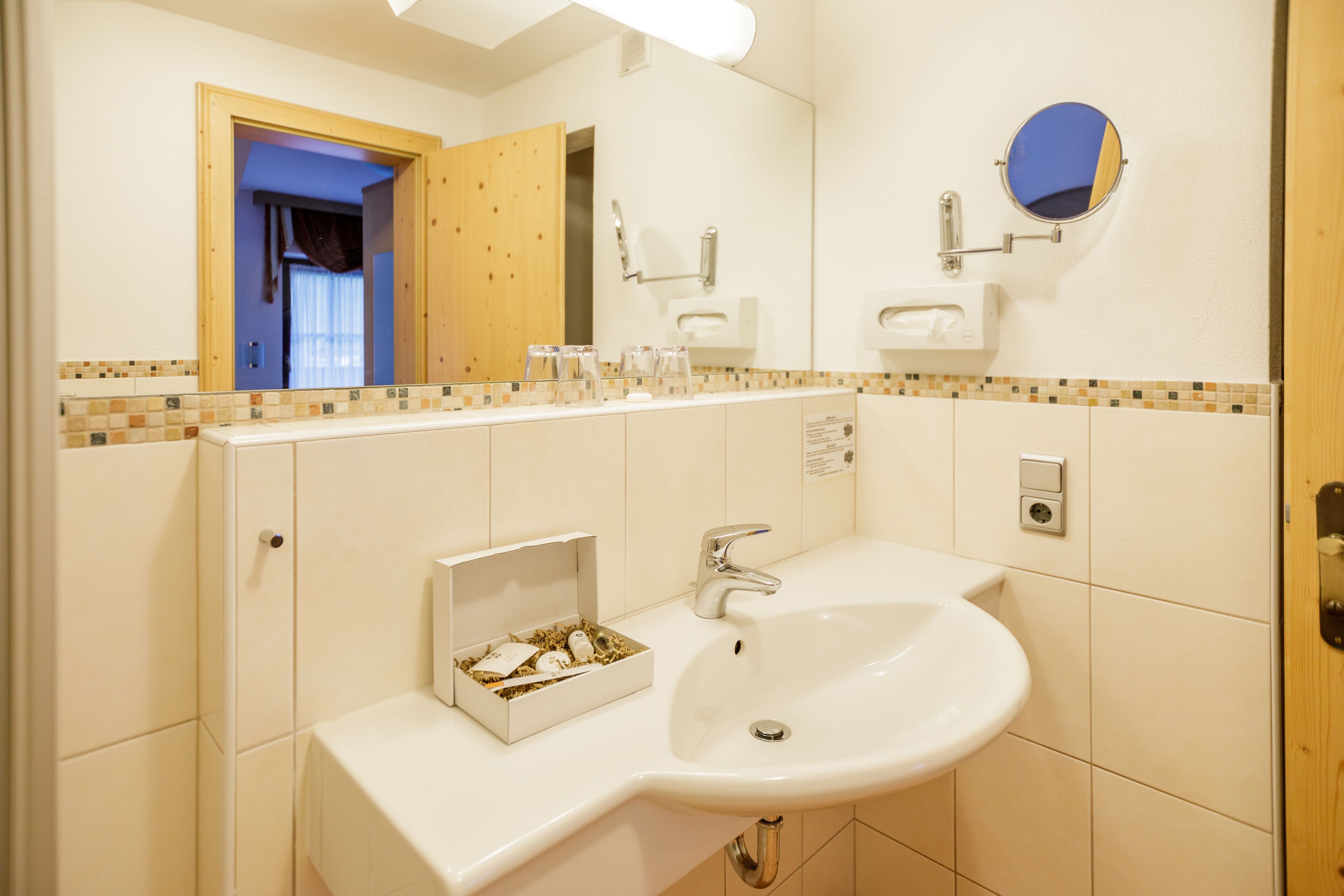 Une salle de bain avec un lavabo blanc, un miroir et une petite boîte contenant des articles de toilette.