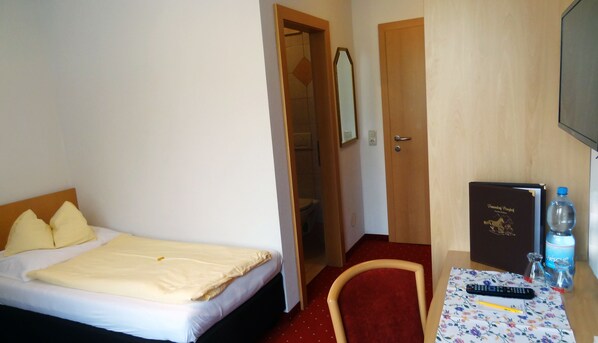 A hotel room with a bed, a desk with a remote control, a water bottle, and a book on the table. - Feriendorf Ponyhof (Fusch an der Grossglocknerstrasse)