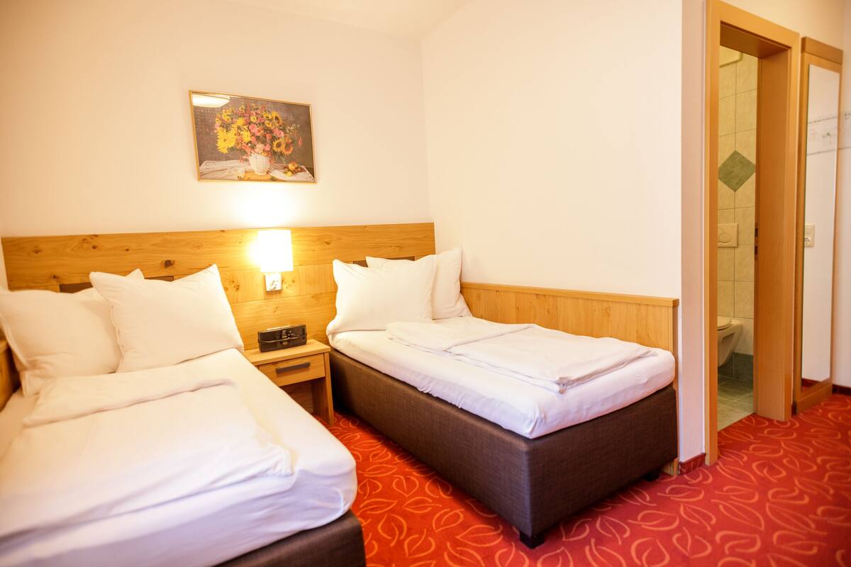 A hotel room with two beds, a wooden headboard, a painting on the wall, and a red patterned carpet.