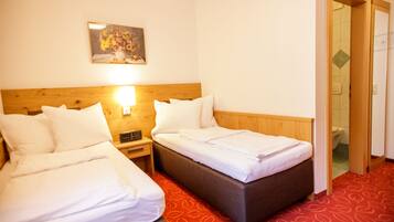 A hotel room with two beds, a wooden headboard, a painting on the wall, and a red patterned carpet.
