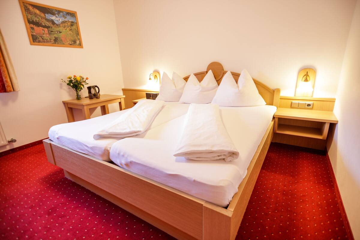 A neatly made bed with white linens and pillows, a wooden headboard, and two bedside tables with lamps.