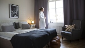 Una habitación de hotel con cama, una silla, una mesita de noche con lámpara y una ventana con cortinas.