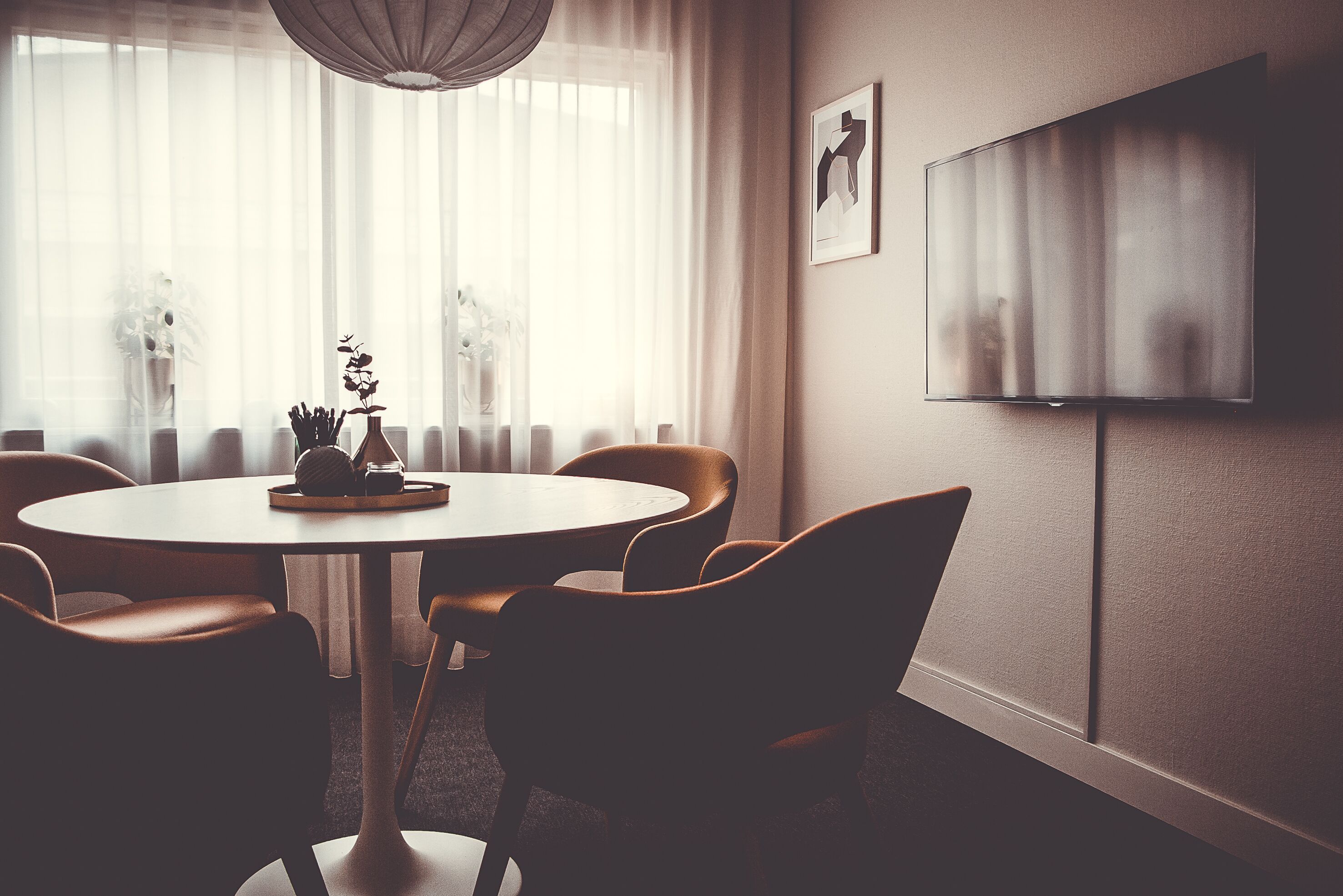 A modern dining area with a round table, leather chairs, a vase with flowers, and a painting on the wall.