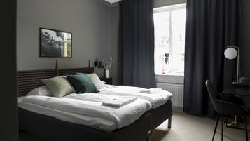 Una cama bien hecha con almohadas, una mesita de noche con lámpara y una ventana con cortinas.