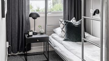 Een slaapkamer met een stapelbed, een raam, een nachtkastje met lamp en een kleine plant.