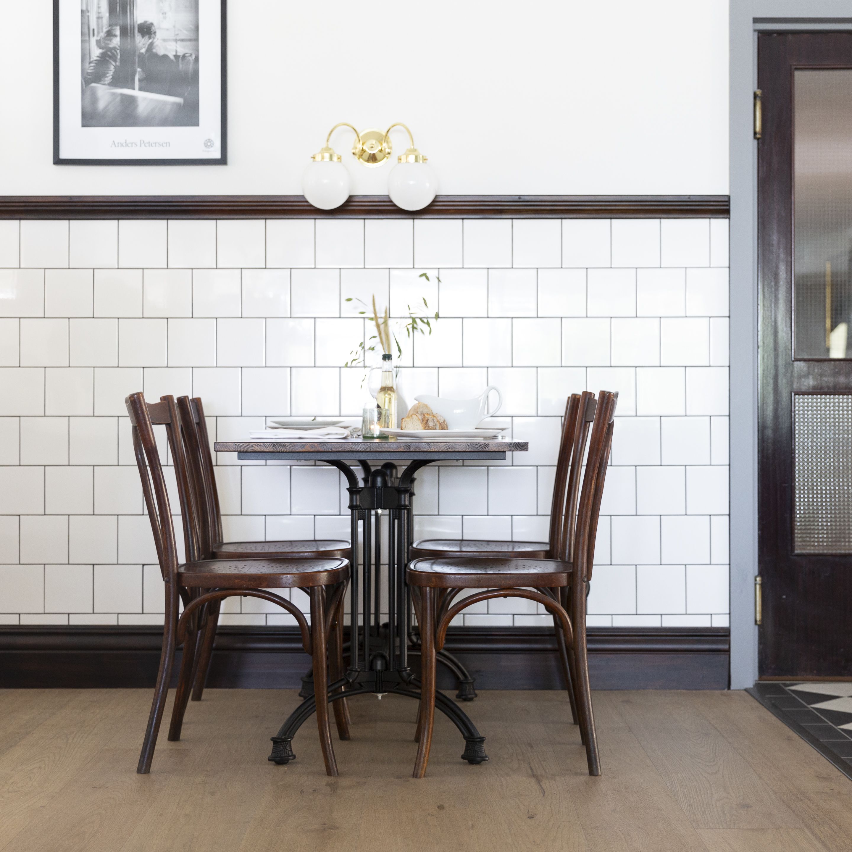 Un comedor con una mesa y cuatro sillas, un protector de salpicaduras blanco de azulejos y un cuadro enmarcado sobre la mesa.