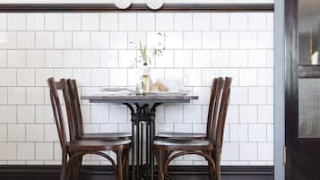 Uma área de refeições com uma mesa e quatro cadeiras, um revestimento de azulejos brancos e um quadro emoldurado acima da mesa.