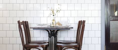 Un comedor con una mesa y cuatro sillas, un protector de salpicaduras blanco de azulejos y un cuadro enmarcado sobre la mesa.