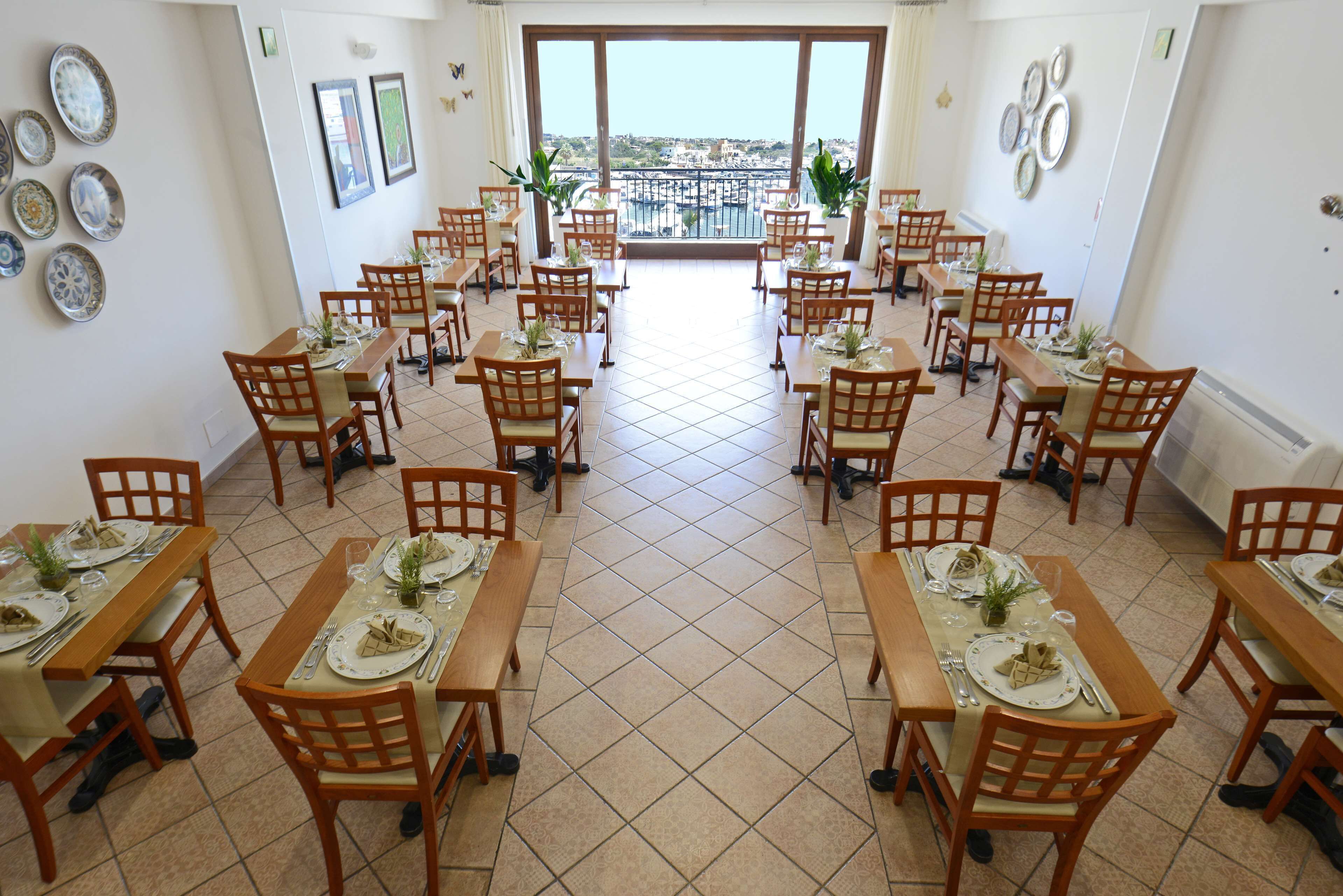 A dining area with multiple tables and chairs, a tiled floor, and a view of the city through large windows.