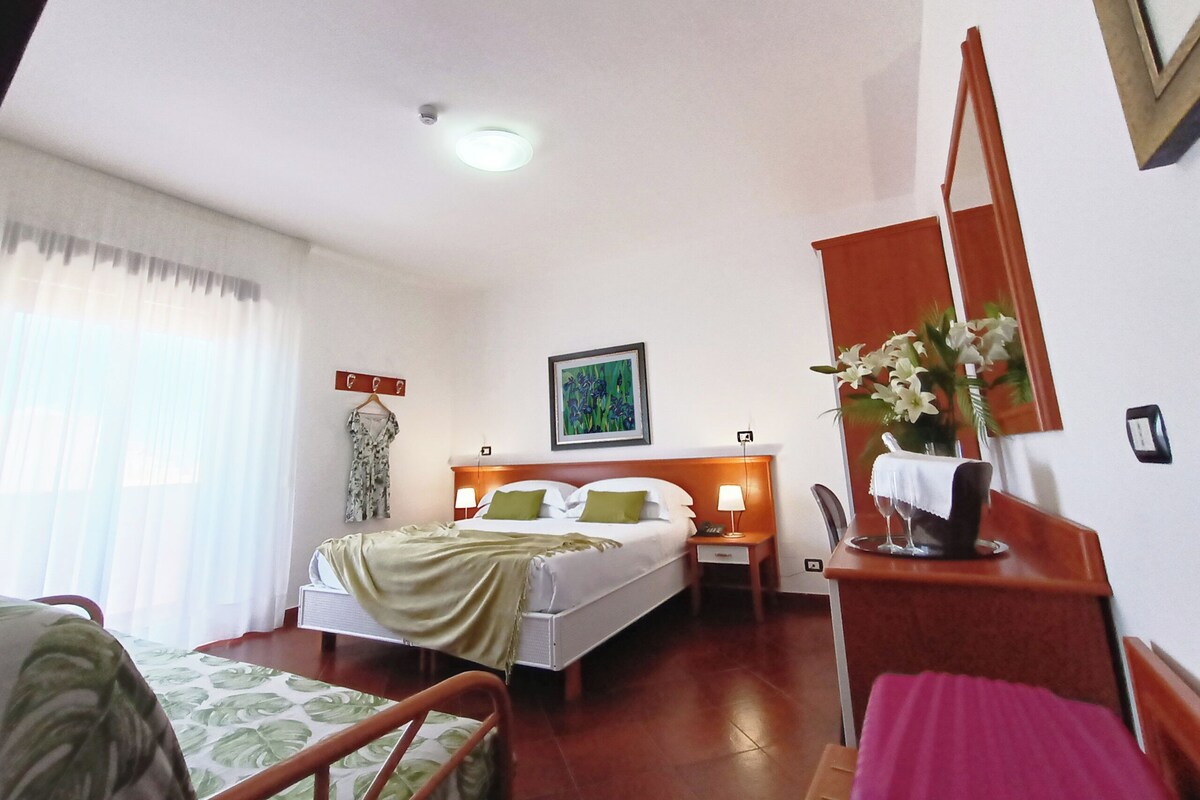 A hotel room with a bed, bedside table, nightstand, and a painting on the wall.
