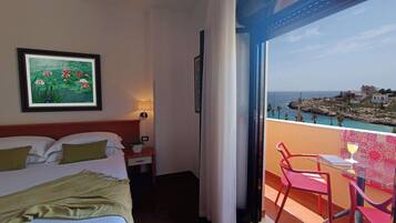 A hotel room with a bed, a nightstand, a lamp, a framed picture, and a balcony with a table and chairs.