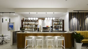 A modern bar area with a central counter, bar stools, and shelves stocked with bottles. - Best Western Hotel Martello (Lampedusa)