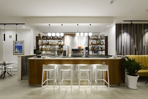 Zona de bar moderna con barra central, taburetes y estantes llenos de botellas.