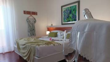 A hotel room with a neatly made bed, a bedside table with a glass of water, a painting on the wall, and a dress on a hanger.