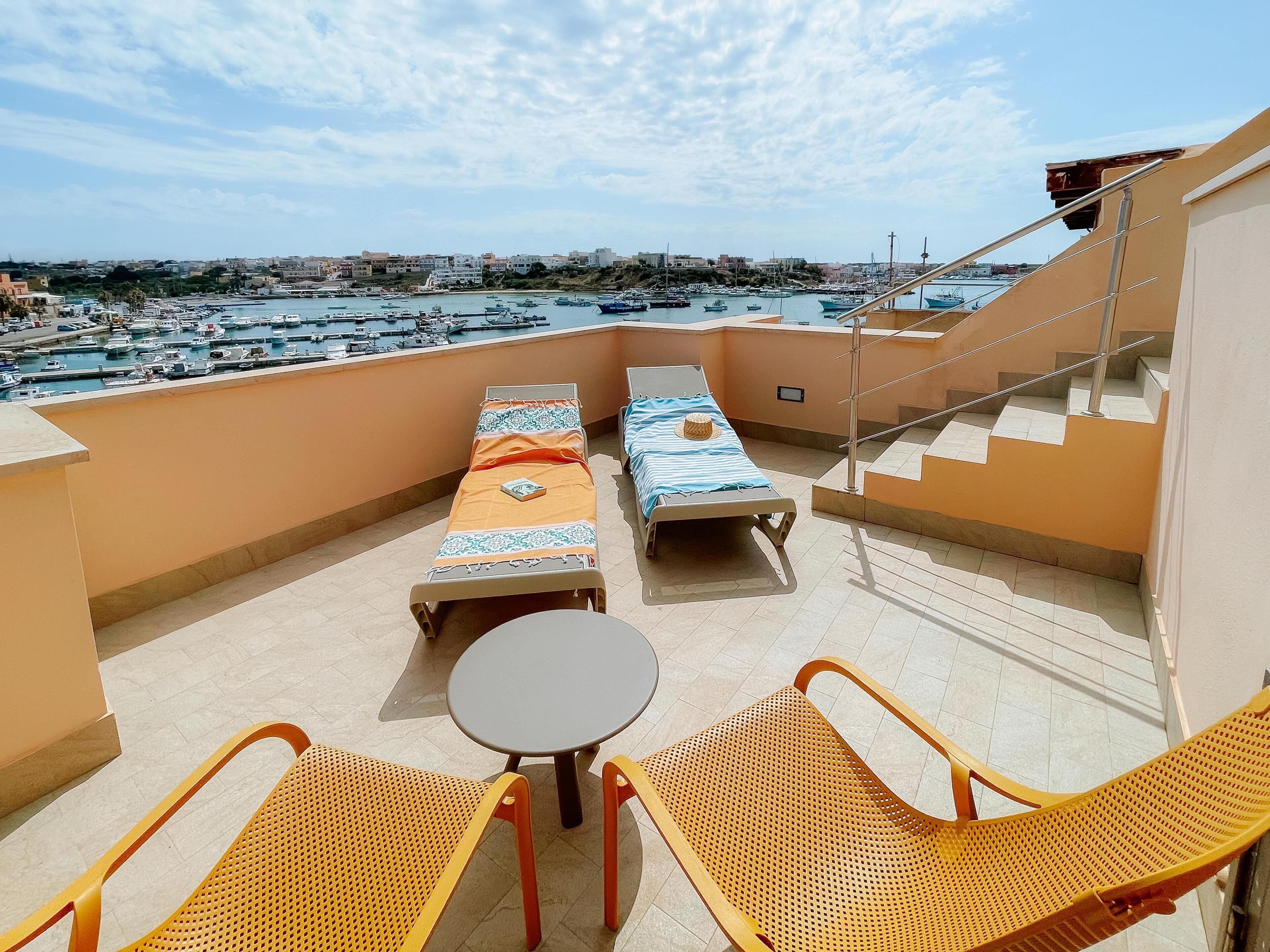 A balcony with two lounge chairs, a small table, and a view of a marina with boats.