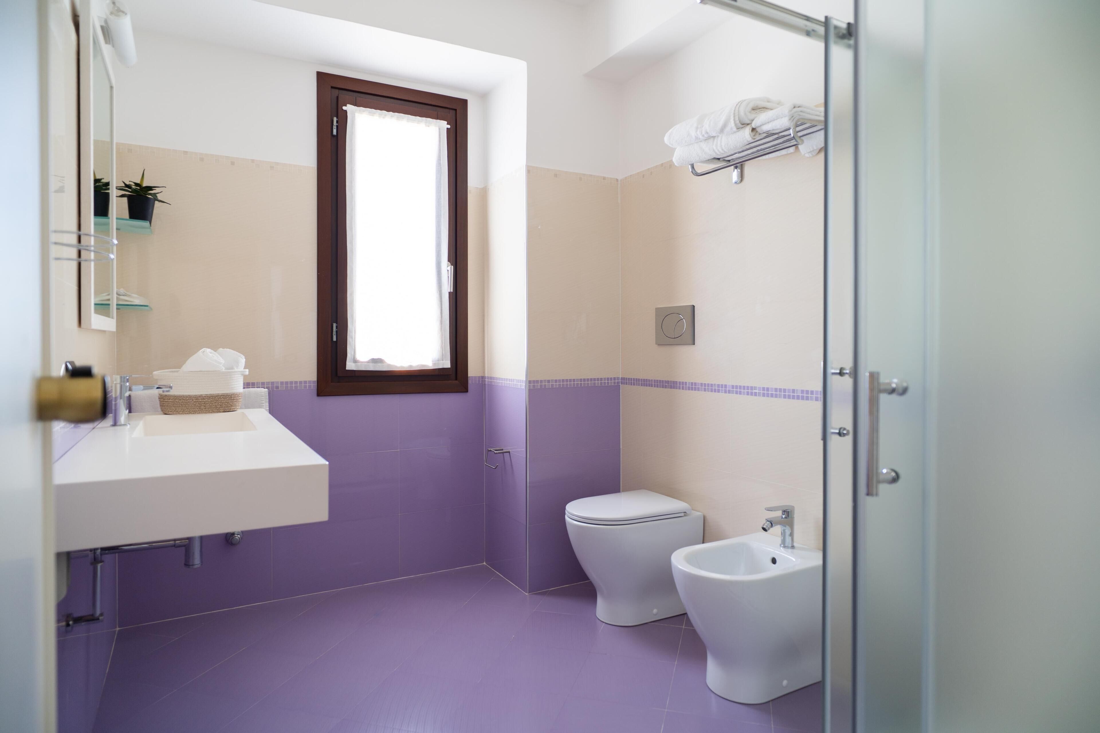 A bathroom with a sink, toilet, bidet, and a window.