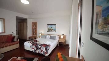 A hotel room with a bed, a sofa, a dining table with oranges, and a painting on the wall.
